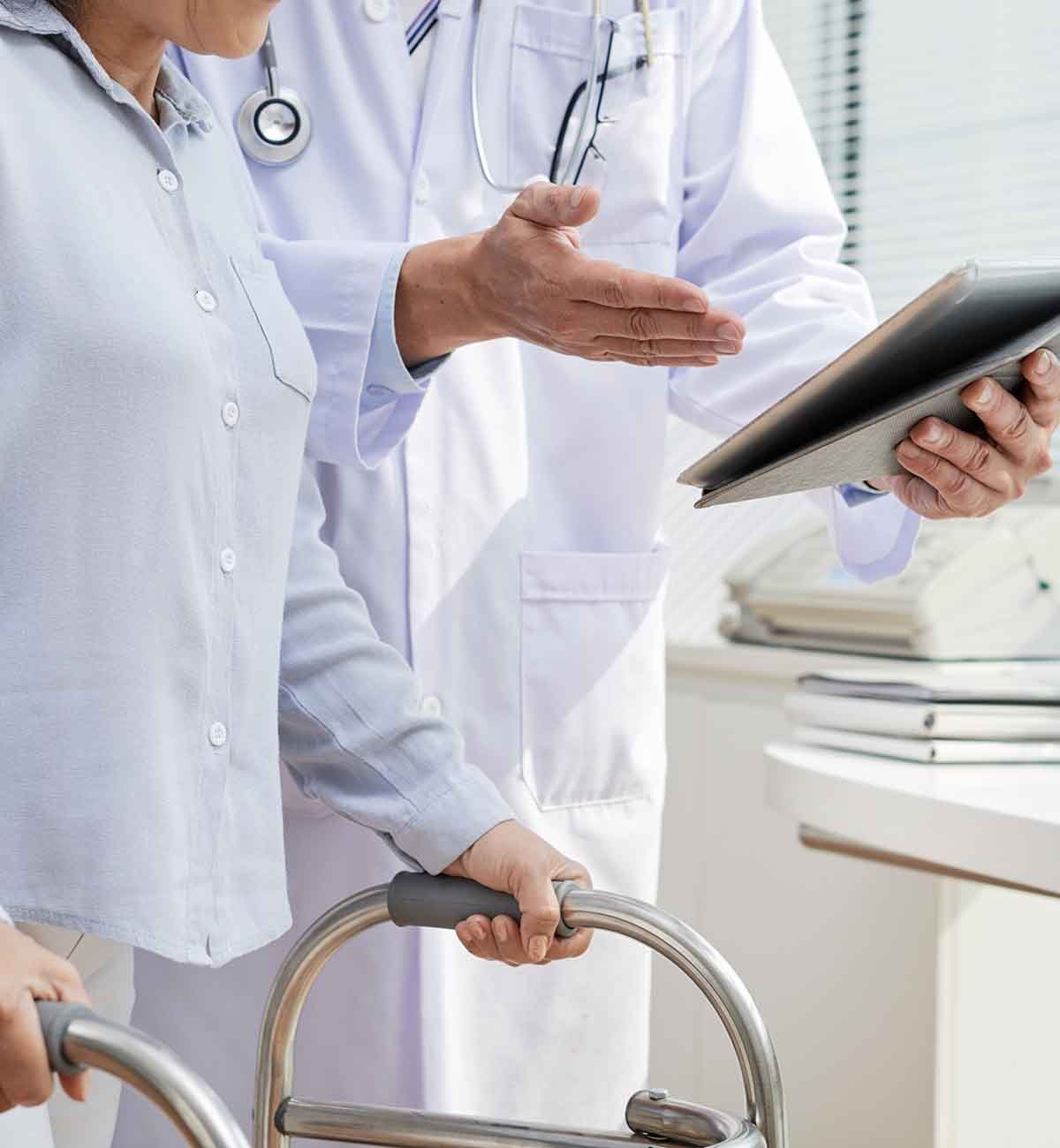 Close-up shot of male physiotherapist wearing white coat using digital tablet while having consultation with traumatize patient